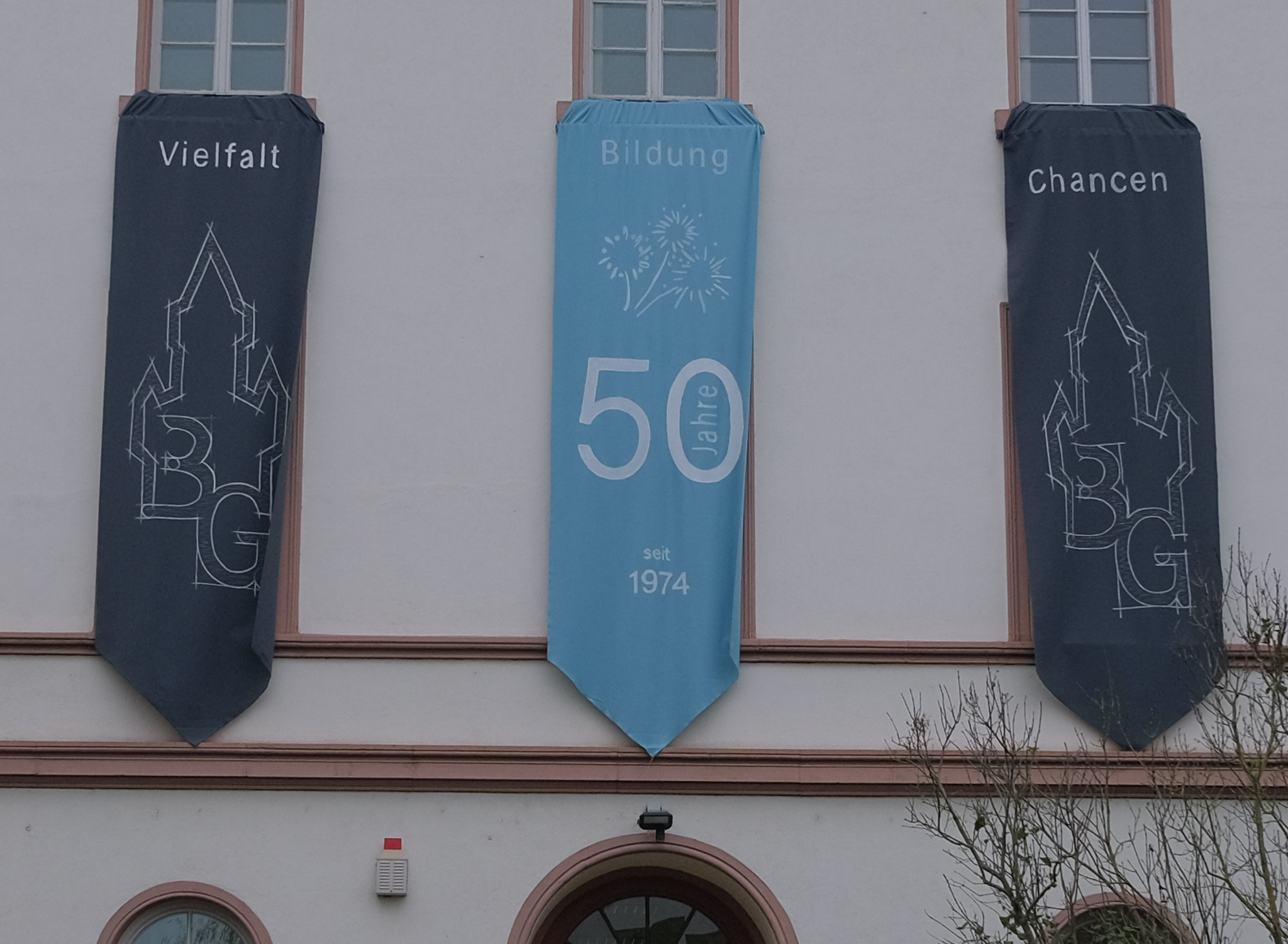 Hier sieht man die festlichen Banner "Vielfalt, Bildung, Chancen" an der Fassade des Burggymnasiums