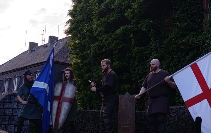 Schauspielszene der englischsprachigen Macbeth-Aufführung auf Schloss Laubach mit Fahnen und Schilden