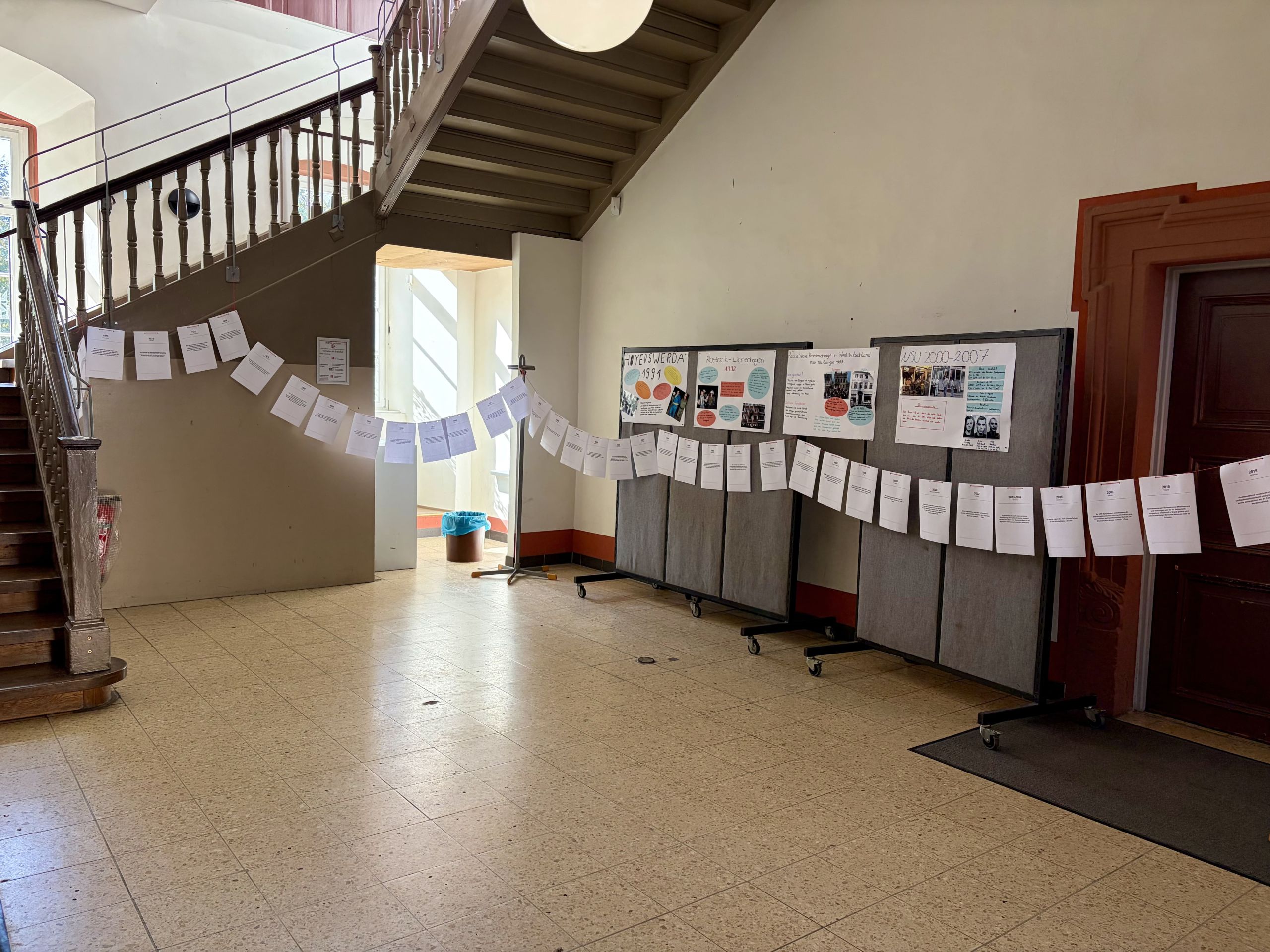 Eine Zeitleiste aus aufgehängten Blättern und Rechercheplakate zu rechter Gewalt im Treppenhaus.